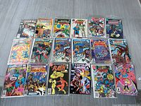 Photo displaying 18 vintage comic books laid out on a table, featuring Spider-Man, Justice League, Superman, Captain America, Flash, Hawkman, and more. Most comics are encased in plastic sleeves.