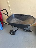 Full side view of the Yardworks wheelbarrow showing the black tray, handles and the tires including the flat front tire.