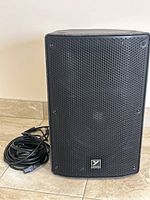 Front view of Yorkville speaker with power cord and microphone cable coiled beside it on tiled floor