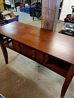 Front angle showing the long wooden side table with four drawers and open shelf below the tabletop.