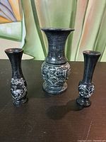 Front view of three carved Chinese marble vases on a dark surface.