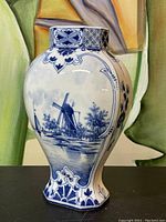 Front view of a ceramic pottery vase showing a blue and white painted Dutch windmill and landscape scene with floral accents.