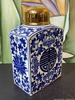 Front and side view of blue and white Chinese porcelain decanter with gold lid showing intricate floral and longevity symbol patterns.
