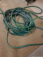 Coiled green garden hose with yellow stripe on floor showing general condition.