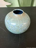 Front side view of round glazed ceramic vase showing crystalline glaze with blue and beige tones.