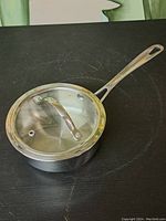 Top angle view of the stainless steel saucepan with lid, showing the long handle and lid handle with vent hole.