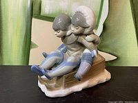 Front angle showing two children on sled, detailed clothing and snow base.