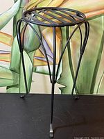 Side view of vintage metal planter stand showing curved tripod legs and round slatted top.