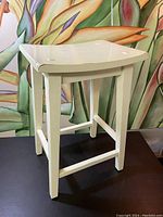 Full view of vintage solid wooden stool painted white with slightly curved seat and inset square accents at corners.