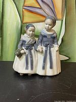 Front view of the Royal Copenhagen porcelain figurine showing two women holding hands and wearing blue and white traditional dresses with a pail.