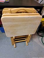 Photo showing four wood folding TV dinner tables stacked together, tabletops are rectangular with rounded corners and foldable legs folded in.