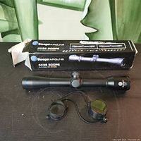 Stoeger 4x32 scope placed on table with original box behind it, showing the scope body and lens caps.