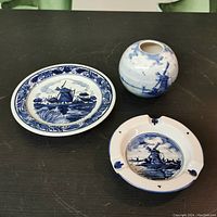 Three blue and white ceramics on black surface showing plate, vase, and ashtray with windmill themes.