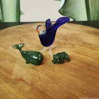Photo showing two green BC jade animal figurines (whale and bear) and one blue glass bird figurine.