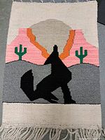 Full view of the woven tapestry showing the entire design of a black coyote silhouette with desert landscape and sunset in the background.
