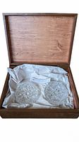 Open wooden box showing the interior with tissue paper and two round cut lead crystal coasters/ashtrays inside.