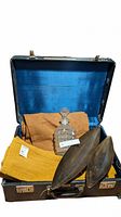 Open antique luggage showing crated and barrel placemats, burnt orange table runner, two decorative bowls and crystal decanter inside.