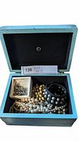 Photo of open blue jewelry box containing pearl necklaces, studded cuff bracelet, and small box with chain jewelry.
