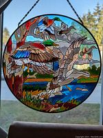 Front view of round stained glass panel showing a vibrant, detailed design of ducks flying over a natural lakeside landscape with a tree on the left and a blue sky background.