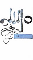 Photo showing four silver spoons, a knife, two bracelets, and two twisted chains arranged with a note indicating sterling silver items.