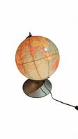 Vintage globe on metal stand unlit, showing detailed map of continents and country borders with electrical cord attached.