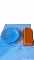 Top view of three periwinkle blue plates stacked and side view of rectangular orange butter dish on white surface with inventory tag visible.