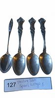 Four vintage sterling silver spoons laid out with visible intricate designs on handles and etched star patterns on the bowls