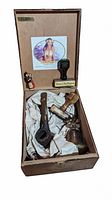 Full view of vintage trinket lot containing pipe, bell, and stamp in wooden box with tissue lining and illustrated lid label