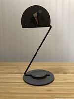Full view of the black and white desk clock with angular wire frame and round base on wooden surface.