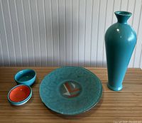 Top down view showing tall turquoise vase, turquoise plate with geometric pattern, and four small bowls in turquoise and orange.