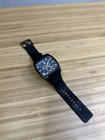 Black DIESEL wristwatch with square face and silicone strap on wooden surface.