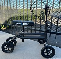 Side view of the entire Knee Rover scooter showing frame, four wheels, padded seat, and handlebar with brake cable.