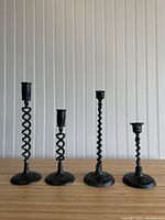 Front view of all four twisted metal candle holders arranged by height on a wooden surface.
