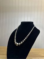 Front angle view of vintage sterling silver round bead necklace on black display bust showing graduated bead sizes and overall design.