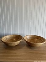 Photo showing both bamboo bowls side by side on a wooden surface against a white paneled wall, highlighting their size and color.