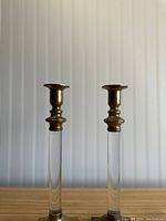 Pair of vintage brass and lucite candle holders side by side showing clear lucite rods, brass tops and square bases.