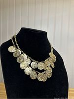 Full view of the gold-colored coin necklace on display stand, showing the layered chain and detailed coin pendants.