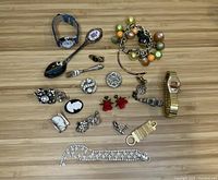 Wide laid out view of vintage jewelry assortment including watches, bracelets, brooches, earrings, rings, and other items on wooden surface