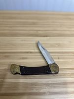 Vintage Ka-Bar folding pocket cutter knife closed showing wooden handle and brass bolsters on wooden surface.