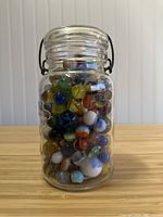 Front view of the glass jar filled with assorted colorful vintage marbles showing various sizes and colors inside.