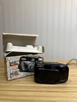 Side view of Minolta Freedom Explorer camera with original box in background, showing dual lens cover and brand name.