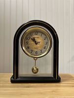 Front view of the vintage Miyabi mantel clock, showing black arched casing, glass panels, gold pendulum, and round dial with Arabic numerals