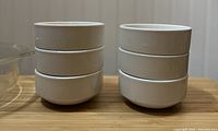 Group photo of six plain white porcelain bowls stacked in two stacks of three each on a wooden surface.