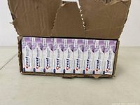 Box partially open showing 28 packs of Crest 3D White toothpaste tubes arranged inside the box.