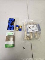 Photo showing multiple brass valve fittings on a white surface, including a sealed box, two small fittings with blue caps, and a plastic bag with multiple fittings.
