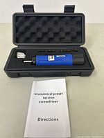 Opened black carrying case showing blue preset torsion screwdriver, assorted bits in foam insert, and instruction manual.