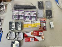 Photo showing toggle bolts packs, black cable ties, outlet boxes, switch plates, fan box covers, Loctite adhesives, and electrical switch in a grouped layout.