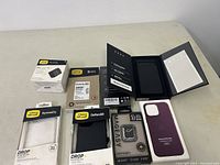Photo of the lot showing multiple new cell phone cases in their packaging including OtterBox and Apple branded cases.