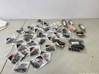 Photo showing multiple small sealed bags of fishing sinkers dispersed on a table with two pink and white fishing lures on the right and several black fishing reel handles clustered.