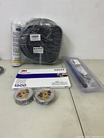 Overall lot with coiled cable packed in plastic, 3M Wetordry abrasive sheet and two rolls of tape, small canister, and clear blister pack with metal parts